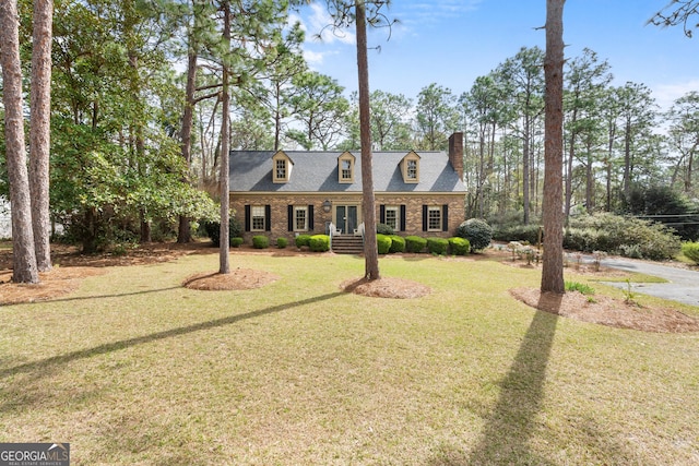 new england style home with a shingled roof, a front yard, brick siding, and a chimney