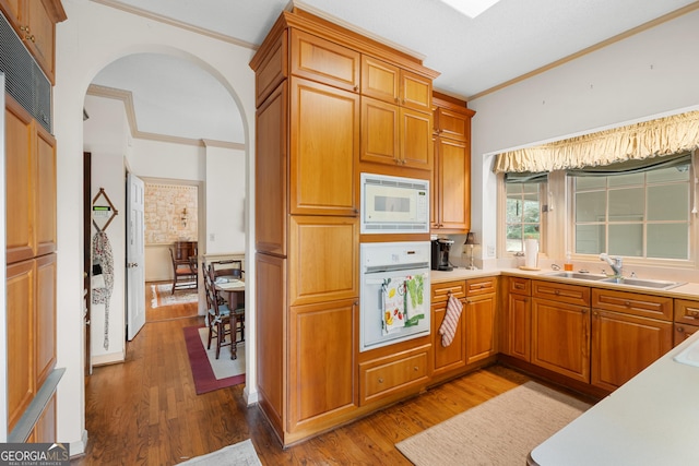 kitchen featuring white appliances, wood finished floors, arched walkways, a sink, and crown molding