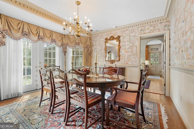 dining space with a notable chandelier, a textured ceiling, wainscoting, and wallpapered walls