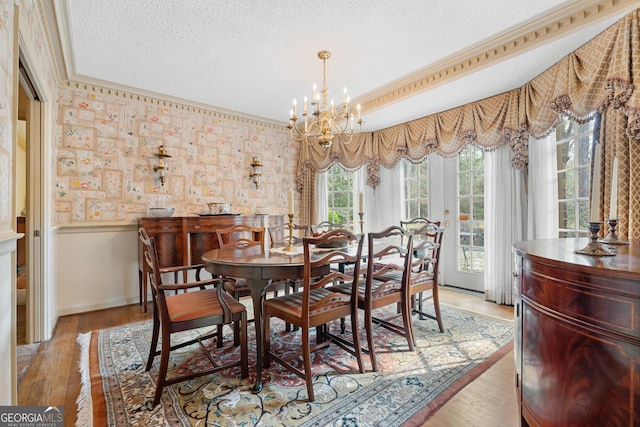 dining space with light wood-type flooring, a notable chandelier, a textured ceiling, and a wainscoted wall