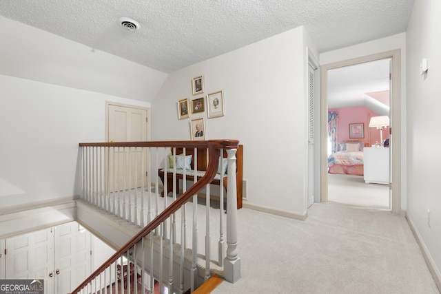 hall featuring visible vents, vaulted ceiling, an upstairs landing, carpet floors, and a textured ceiling