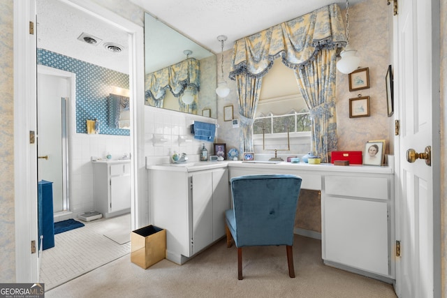 bathroom with wallpapered walls, wainscoting, a textured ceiling, tile walls, and a shower with door