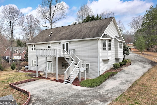 rear view of house featuring stairway, roof with shingles, a wooden deck, concrete driveway, and french doors