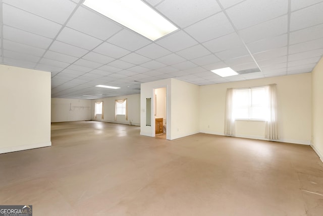 basement featuring a wealth of natural light, a paneled ceiling, and baseboards