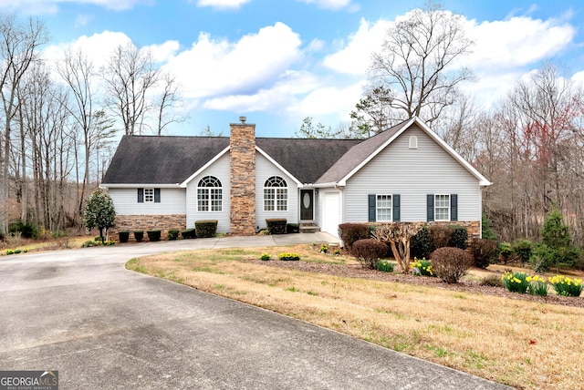 ranch-style house featuring an attached garage, roof with shingles, a chimney, stone siding, and driveway