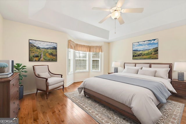 bedroom featuring ceiling fan, baseboards, a raised ceiling, and light wood-style floors