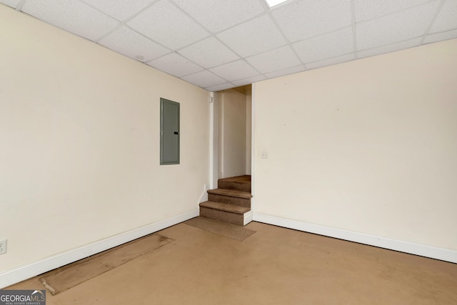 spare room featuring baseboards, electric panel, stairs, a paneled ceiling, and concrete flooring