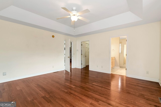 unfurnished bedroom with a tray ceiling, baseboards, wood finished floors, and a spacious closet