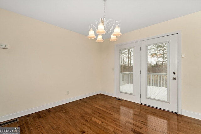 unfurnished dining area featuring an inviting chandelier, wood finished floors, baseboards, and visible vents