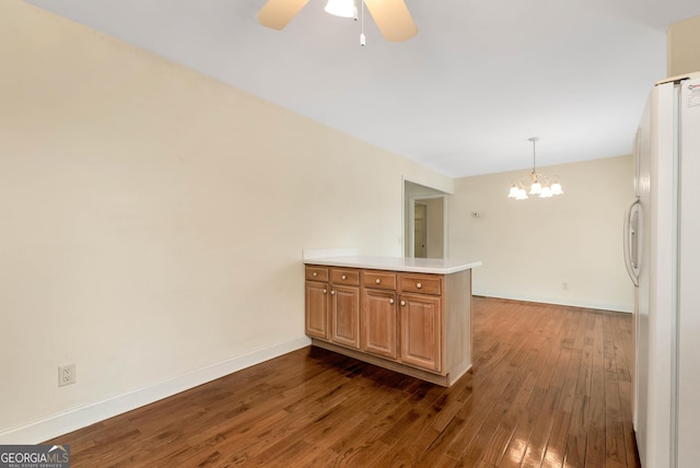 kitchen featuring dark wood-style floors, baseboards, a peninsula, freestanding refrigerator, and ceiling fan with notable chandelier