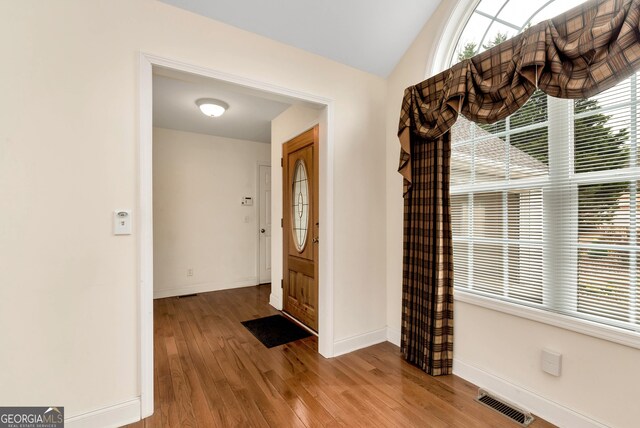 foyer featuring vaulted ceiling, wood finished floors, visible vents, and baseboards