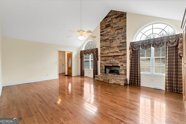 unfurnished living room with baseboards, ceiling fan, a stone fireplace, high vaulted ceiling, and wood-type flooring