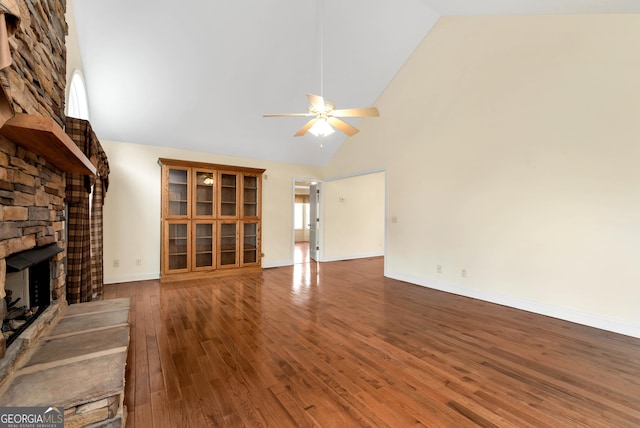 unfurnished living room featuring wood finished floors, baseboards, high vaulted ceiling, a fireplace, and ceiling fan