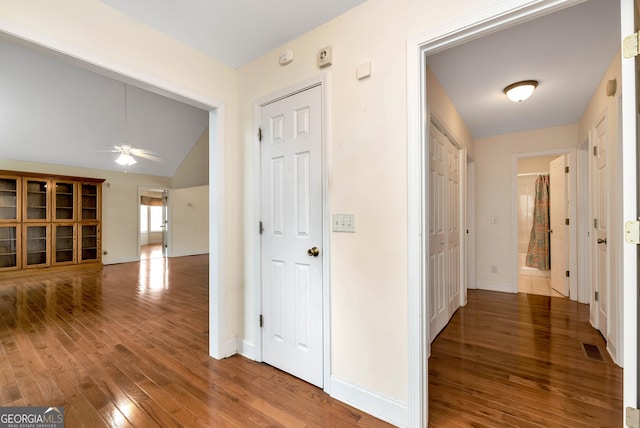 hallway with vaulted ceiling, wood finished floors, visible vents, and baseboards