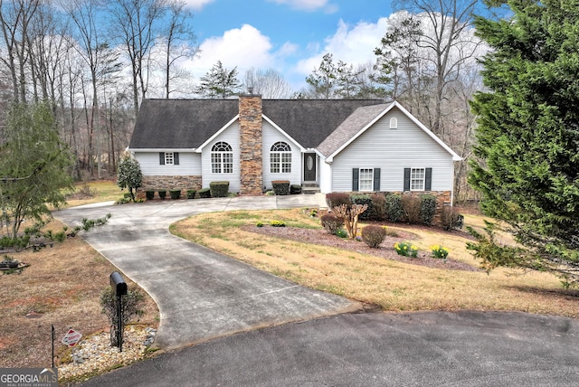 ranch-style home with stone siding, curved driveway, a chimney, and a shingled roof