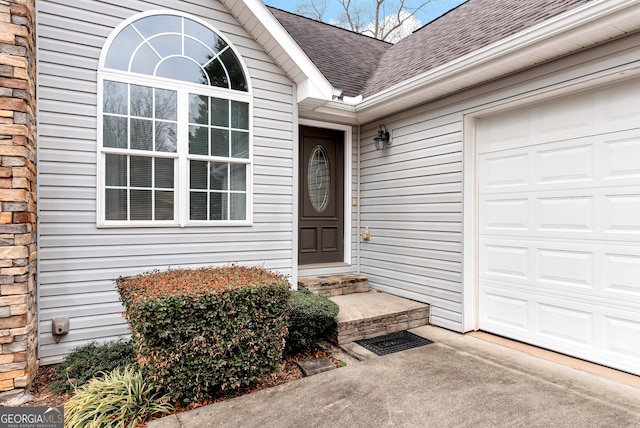 doorway to property featuring driveway, a shingled roof, and a garage