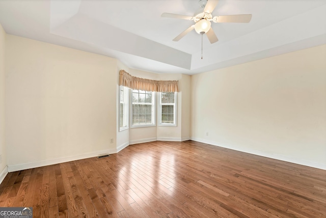 empty room with baseboards, a raised ceiling, hardwood / wood-style floors, and a ceiling fan