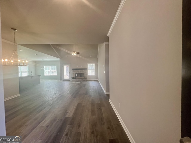 unfurnished living room featuring baseboards, ornamental molding, ceiling fan with notable chandelier, a fireplace, and dark wood-style floors