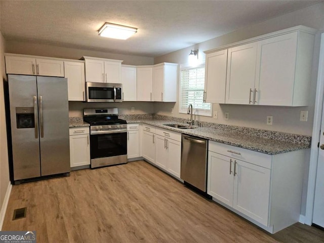147 Mildred Ct, Dallas, GA 30157 - kitchen featuring appliances with stainless steel finishes, light wood-style floors, white cabinetry, light stone countertops, and a textured ceiling