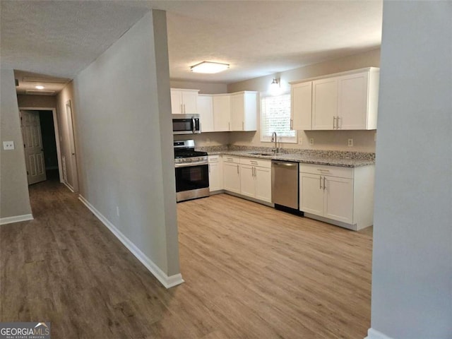 147 Mildred Ct, Dallas, GA 30157 - kitchen featuring stainless steel appliances, light wood finished floors, white cabinetry, light stone countertops, and a textured ceiling