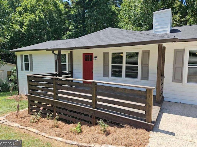 ranch-style house featuring a shingled roof, a porch, and a chimney