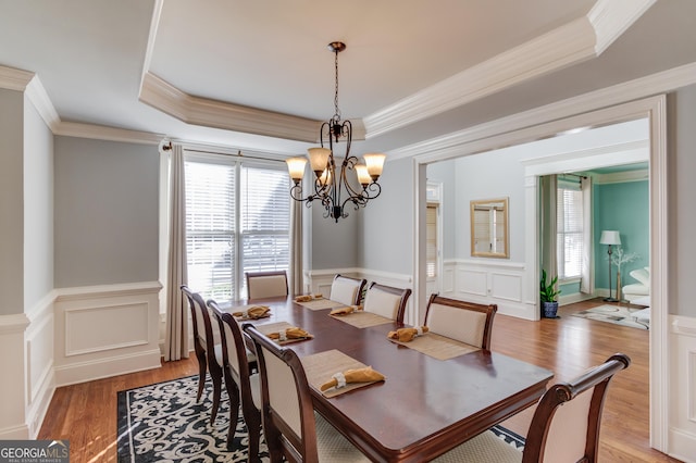 dining room with a raised ceiling, light wood-type flooring, a wealth of natural light, and a chandelier