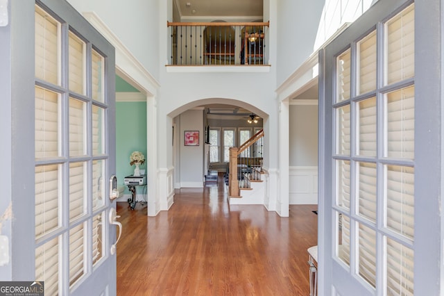 entryway featuring wood finished floors, stairway, arched walkways, a high ceiling, and wainscoting