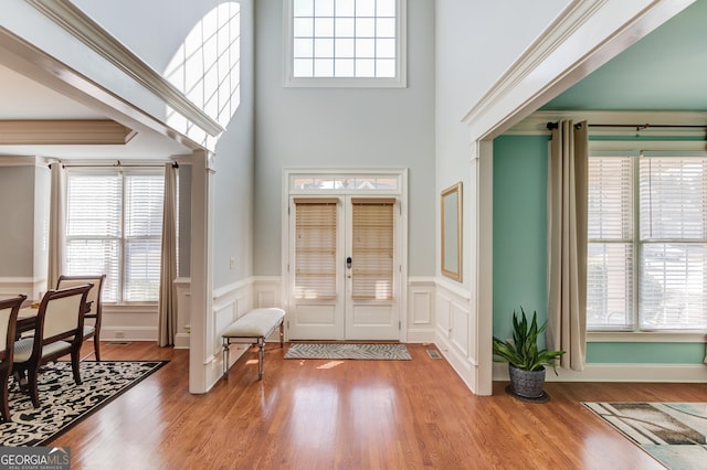 foyer entrance with wood finished floors, a wainscoted wall, a high ceiling, crown molding, and a decorative wall