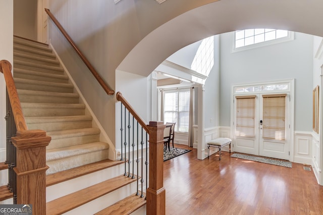 foyer entrance with arched walkways, stairway, wainscoting, and wood finished floors