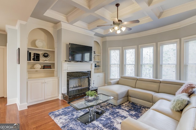 living area featuring a ceiling fan, coffered ceiling, light wood finished floors, a premium fireplace, and beam ceiling