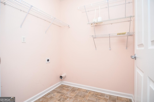 clothes washing area with laundry area, electric dryer hookup, stone finish flooring, and baseboards