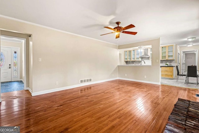 unfurnished living room with hardwood / wood-style flooring, ornamental molding, baseboards, and ceiling fan