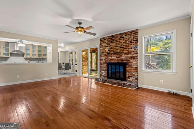 unfurnished living room with a brick fireplace, baseboards, hardwood / wood-style floors, a ceiling fan, and a sink