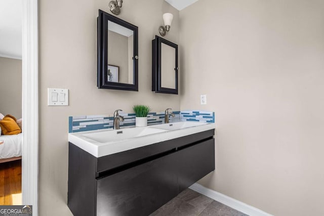 full bathroom with ensuite bathroom, a sink, tasteful backsplash, double vanity, and baseboards