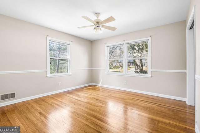 empty room featuring ceiling fan, wood finished floors, visible vents, and baseboards