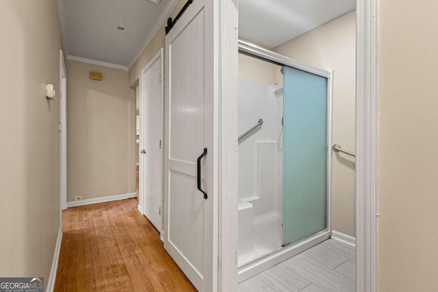 bathroom featuring a shower stall, wood finished floors, baseboards, and ornamental molding