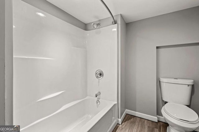 bathroom with bathing tub / shower combination, toilet, wood finished floors, and baseboards