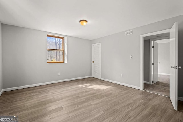 unfurnished bedroom with wood finished floors, visible vents, a closet, and baseboards