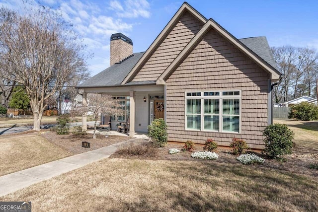 view of front of property with a chimney, a front yard, and a shingled roof