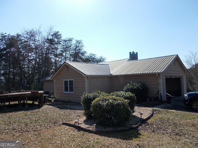 view of side of home with metal roof, a garage, a chimney, and a standing seam roof