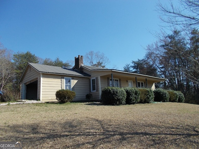 view of front of home featuring a front lawn, a chimney, a garage, and metal roof