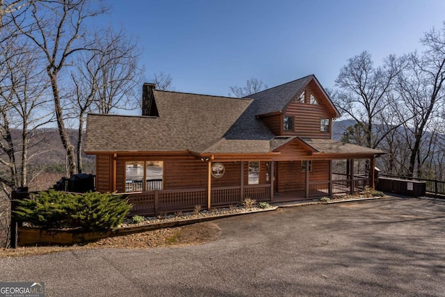 rustic home with log veneer siding, aphalt driveway, covered porch, and a shingled roof