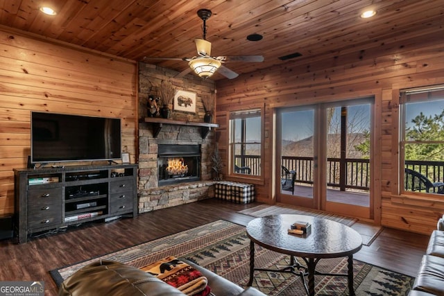 living room with wooden walls, ceiling fan, wood ceiling, a fireplace, and wood finished floors