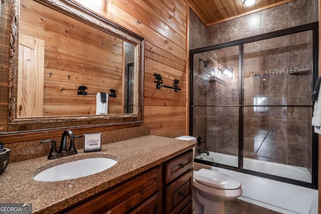 bathroom featuring bath / shower combo with glass door, wooden walls, vanity, and toilet