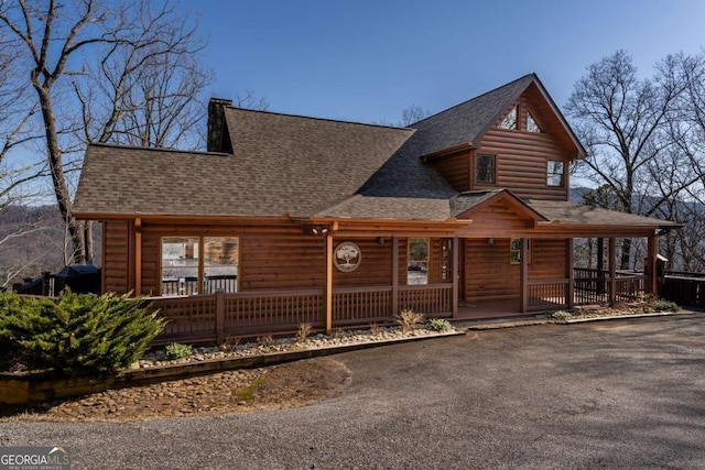 view of front of home featuring log veneer siding, aphalt driveway, roof with shingles, and covered porch