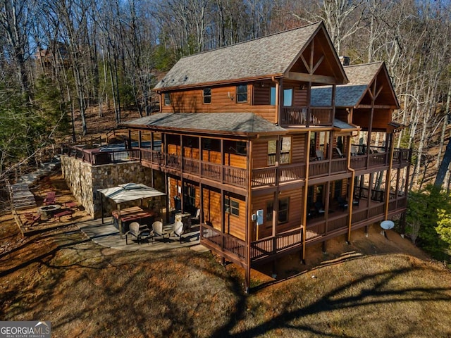 back of property with a shingled roof, a yard, a balcony, log veneer siding, and a patio