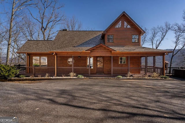 view of front facade with faux log siding, a chimney, covered porch, and a shingled roof