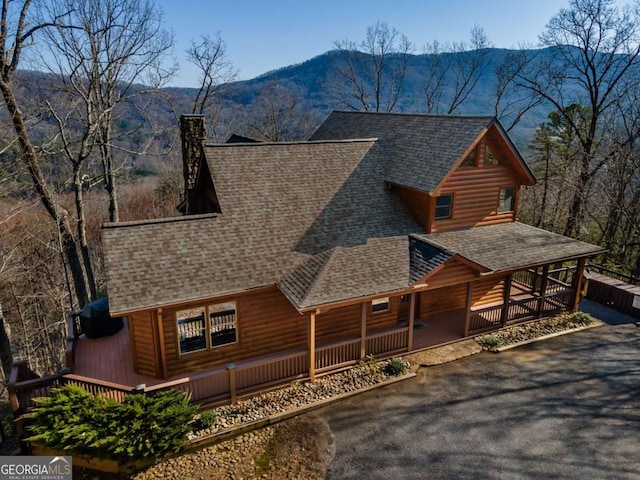 view of front of home with a chimney, a deck with mountain view, a shingled roof, and log veneer siding