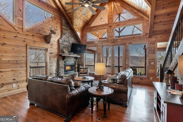 living area with hardwood / wood-style floors, wooden walls, a stone fireplace, wooden ceiling, and ceiling fan