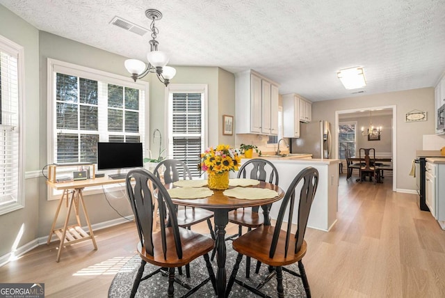 dining room featuring visible vents, baseboards, a chandelier, light wood-style floors, and a textured ceiling